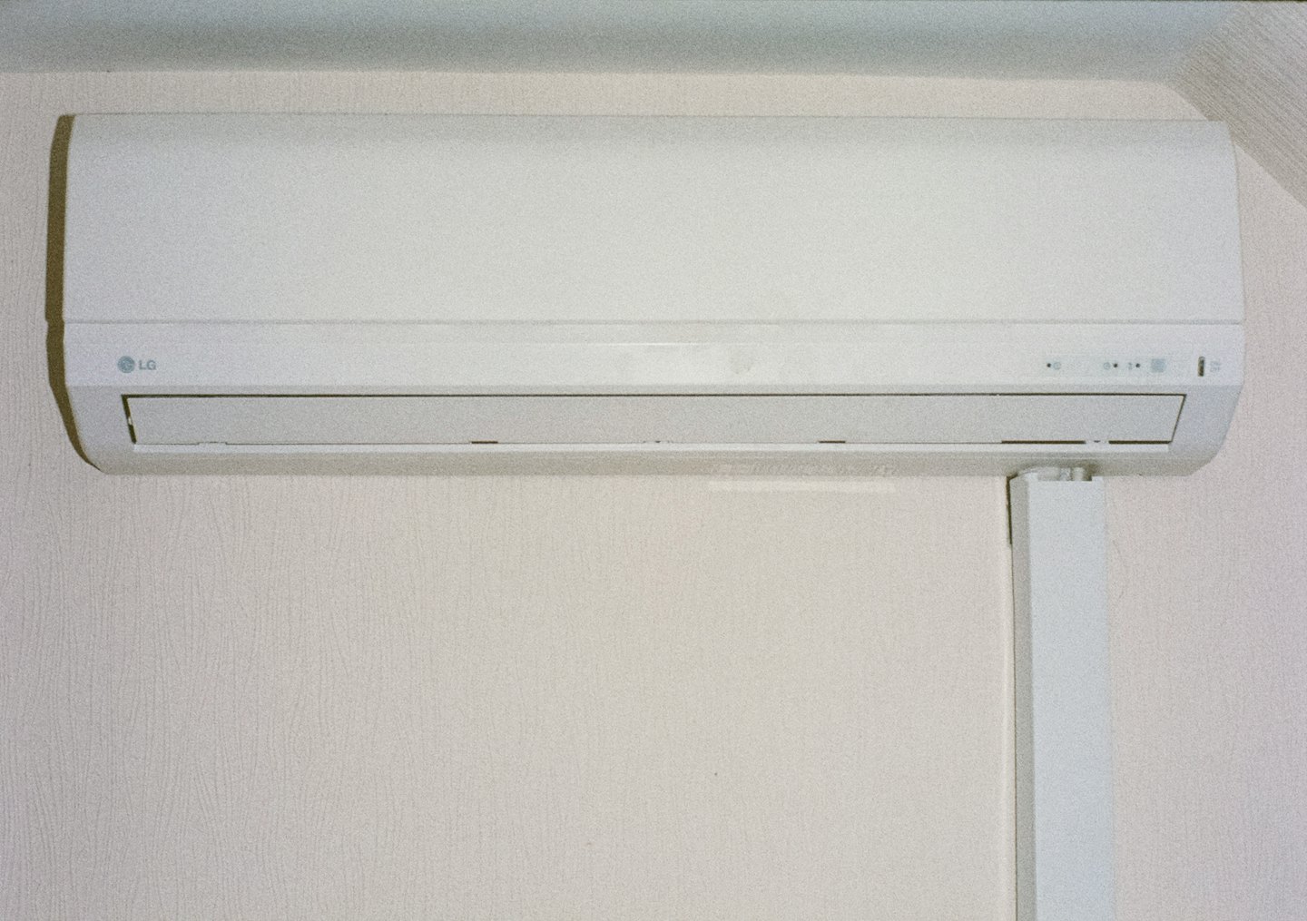 Nástenná klimatizačná jednotka s bielym potrubím na textúrovanej tapete.